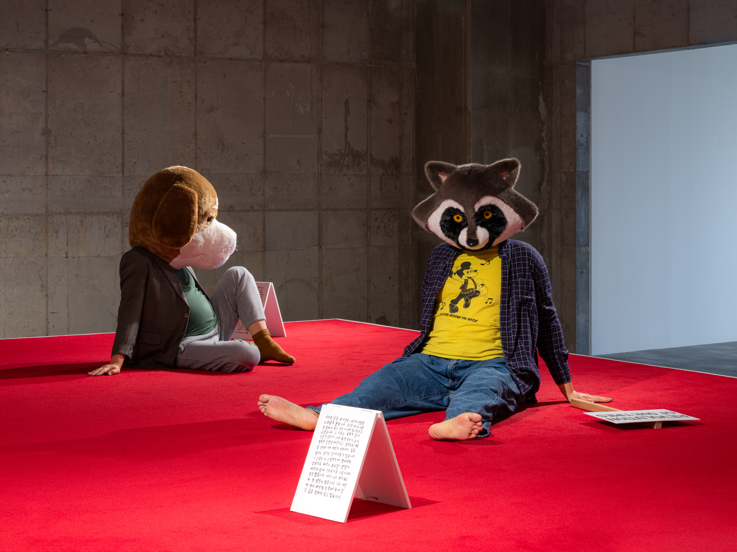  김홍석, 침묵의 고독-망명자, 2019, 레진, 스펀지, 옷, 천, 목재 플래카드, 101×105×131cm, 목재 플래카드: 64×35cm, 소개문: 31×21cm